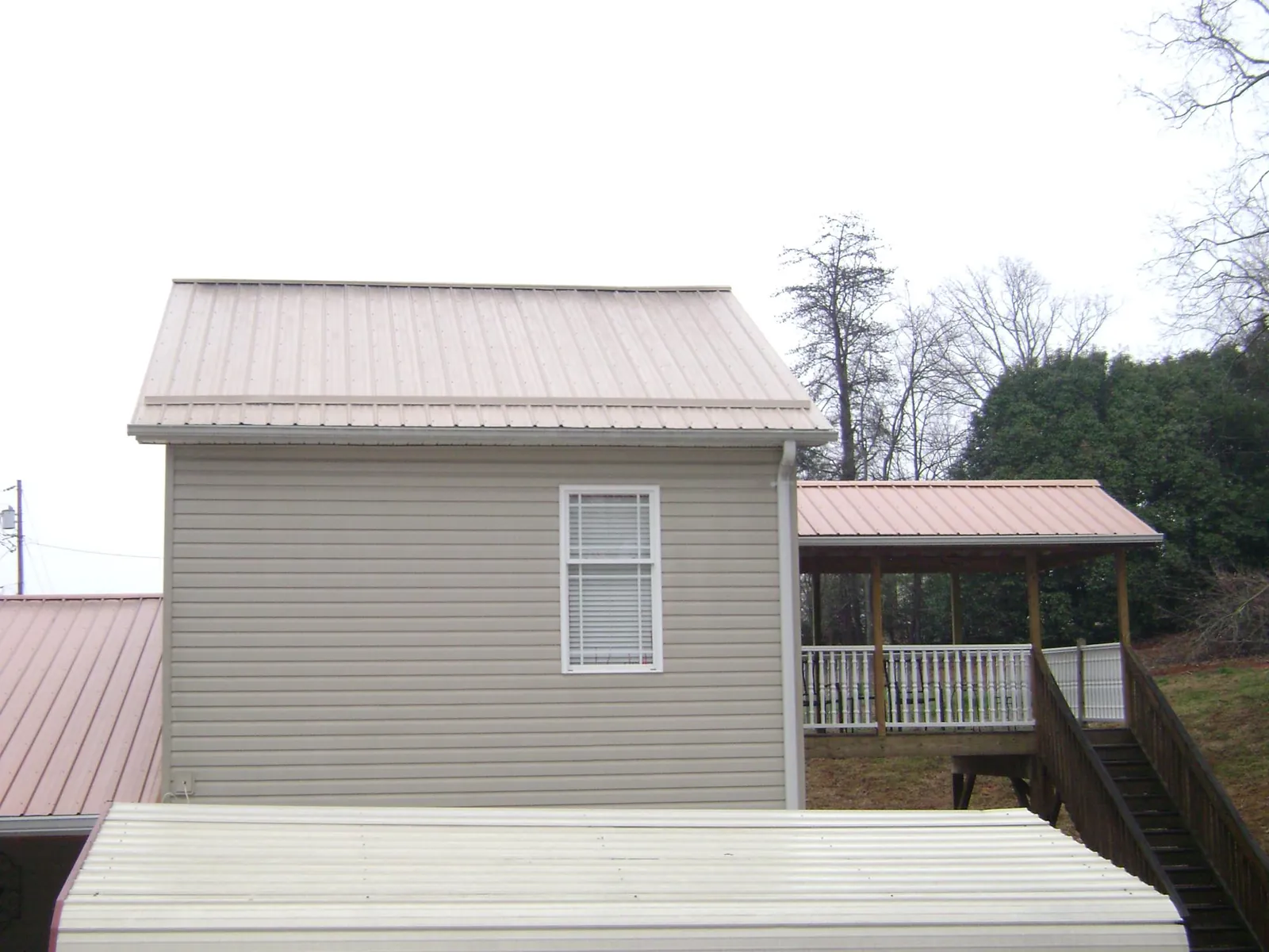 Tan metal roofs on a two story addition and attached porch, from a Roof Replacement job in Hammond